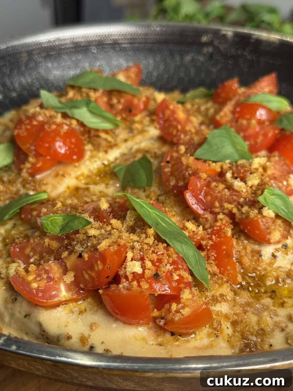 Crispy Baked Chicken Parm with Light Marinara 2 A close-up of a pan with cooked chicken breasts topped with chopped cherry tomatoes, crispy breadcrumbs, and fresh basil leaves. The dish appears juicy and garnished, ready to serve.