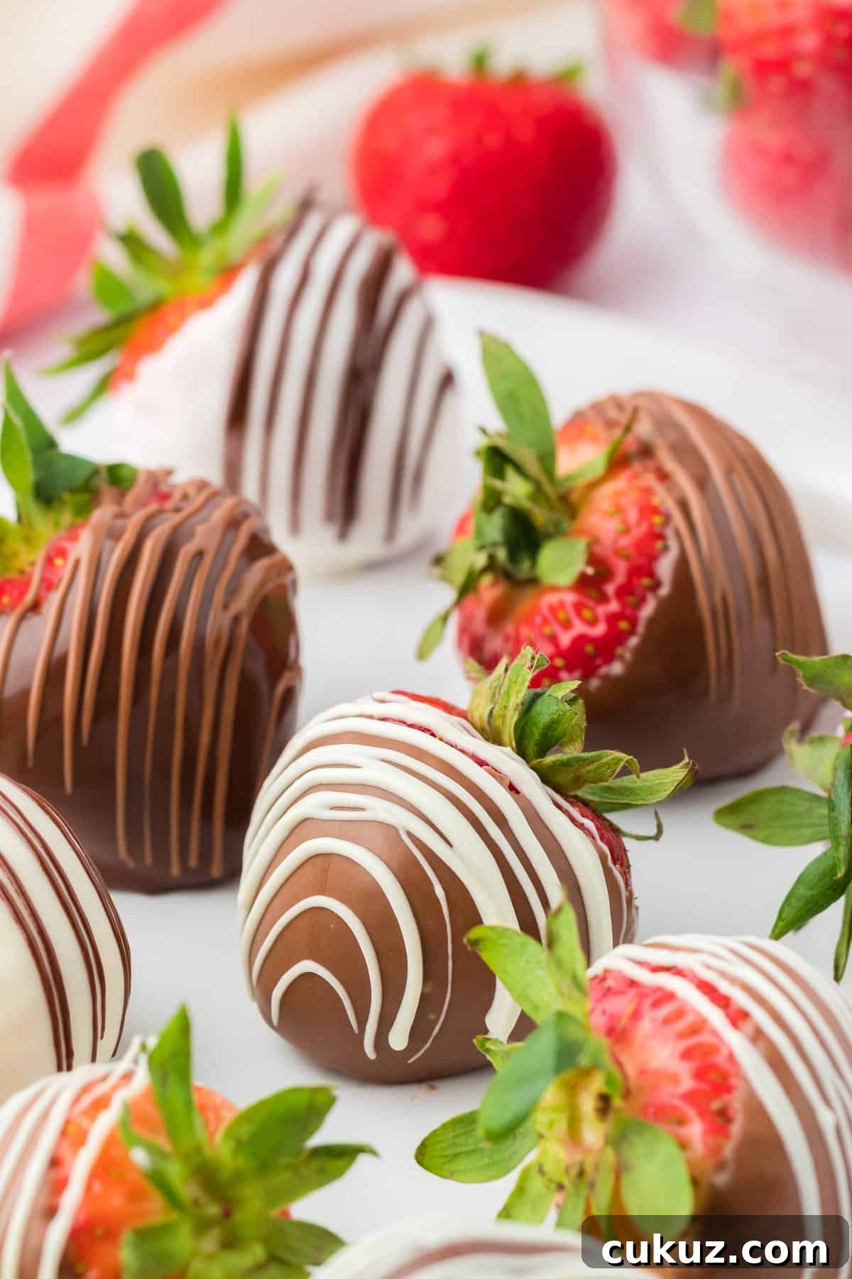 close up of a chocolate covered strawberry with a white chocolate drizzle, surrounded by more chocolate strawberries