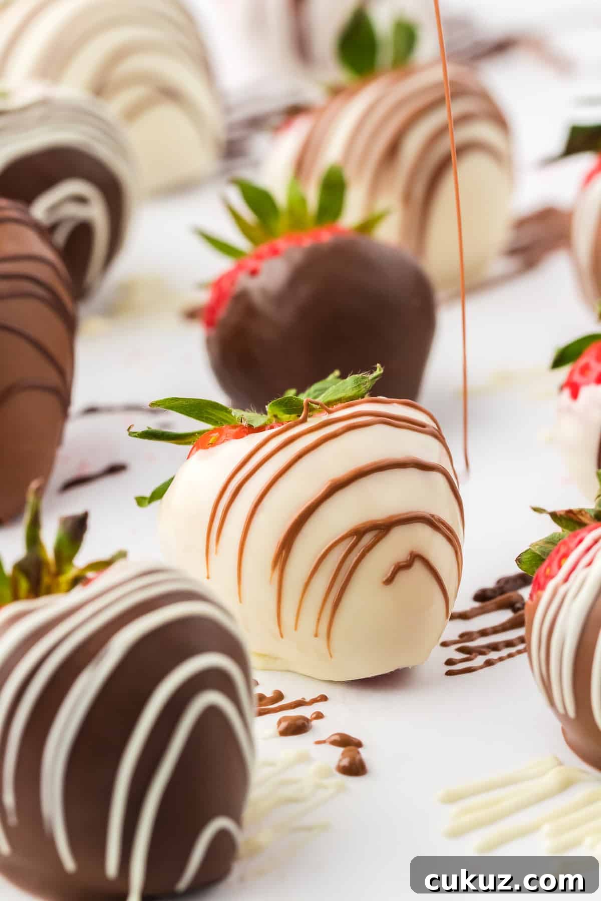 a white chocolate covered strawberry being drizzled with milk chocolate, surrounded by more chocolate covered strawberries