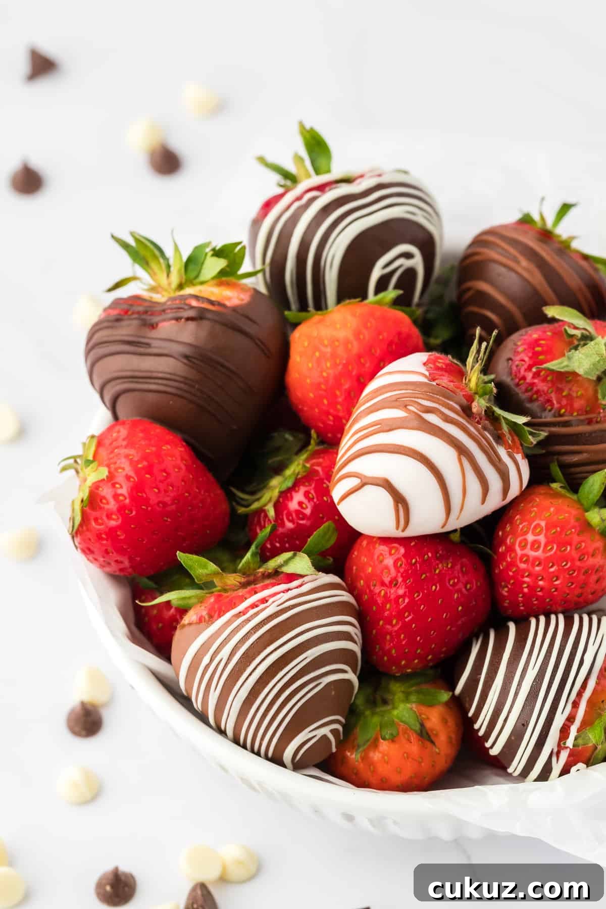 a white bowl full of chocolate covered strawberries and fresh strawberries surrounded by white and milk chocolate chips