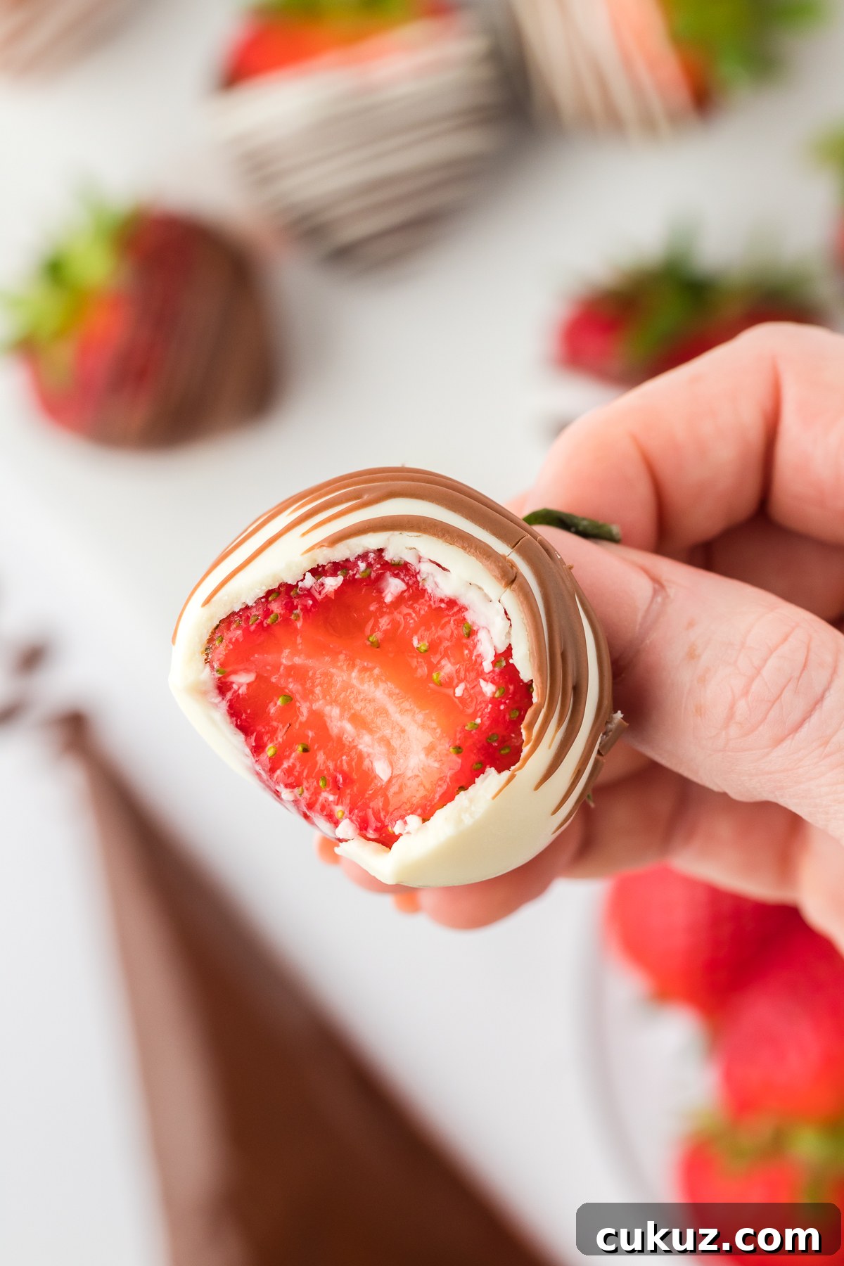 Close up of a hand holding a chocolate covered strawberry with one bite out of it, showing the fresh red strawberry inside