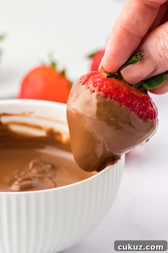 A strawberry that has been dipped into a bowl of chocolate being run along the inner edge of the bowl to remove excess chocolate