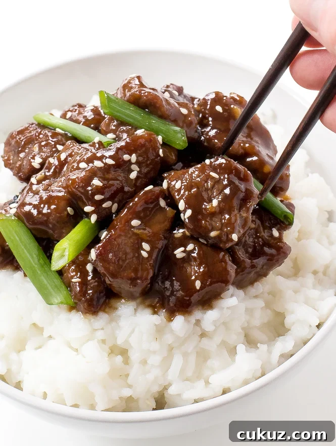 Delicious Mongolian beef on white rice, garnished with green onions and sesame seeds.