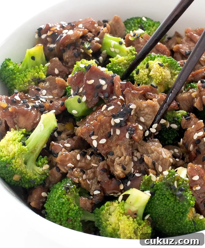 Beef and broccoli recipe in a large white bowl. Topped with sauce and sesame seeds.