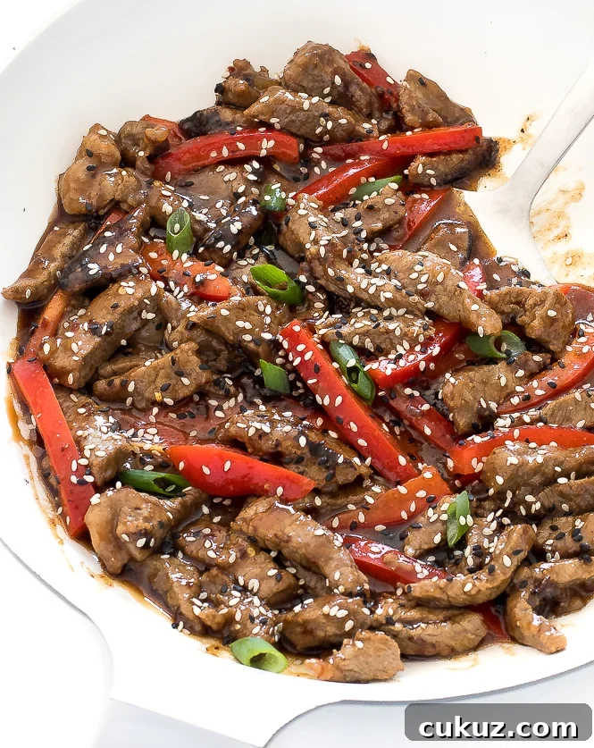 Delicious spicy Szechuan beef recipe with red bell pepper, green onions and sesame seeds in a large skillet.