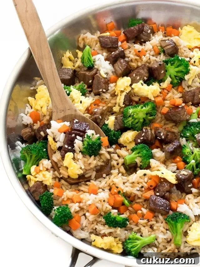 Beef fried rice in pan with wooden spoon and veggies.