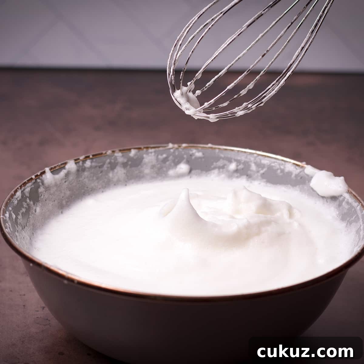 Someone lifting a whisk from a bowl of beaten egg whites to show that the egg whites are at the stiff peak stage.