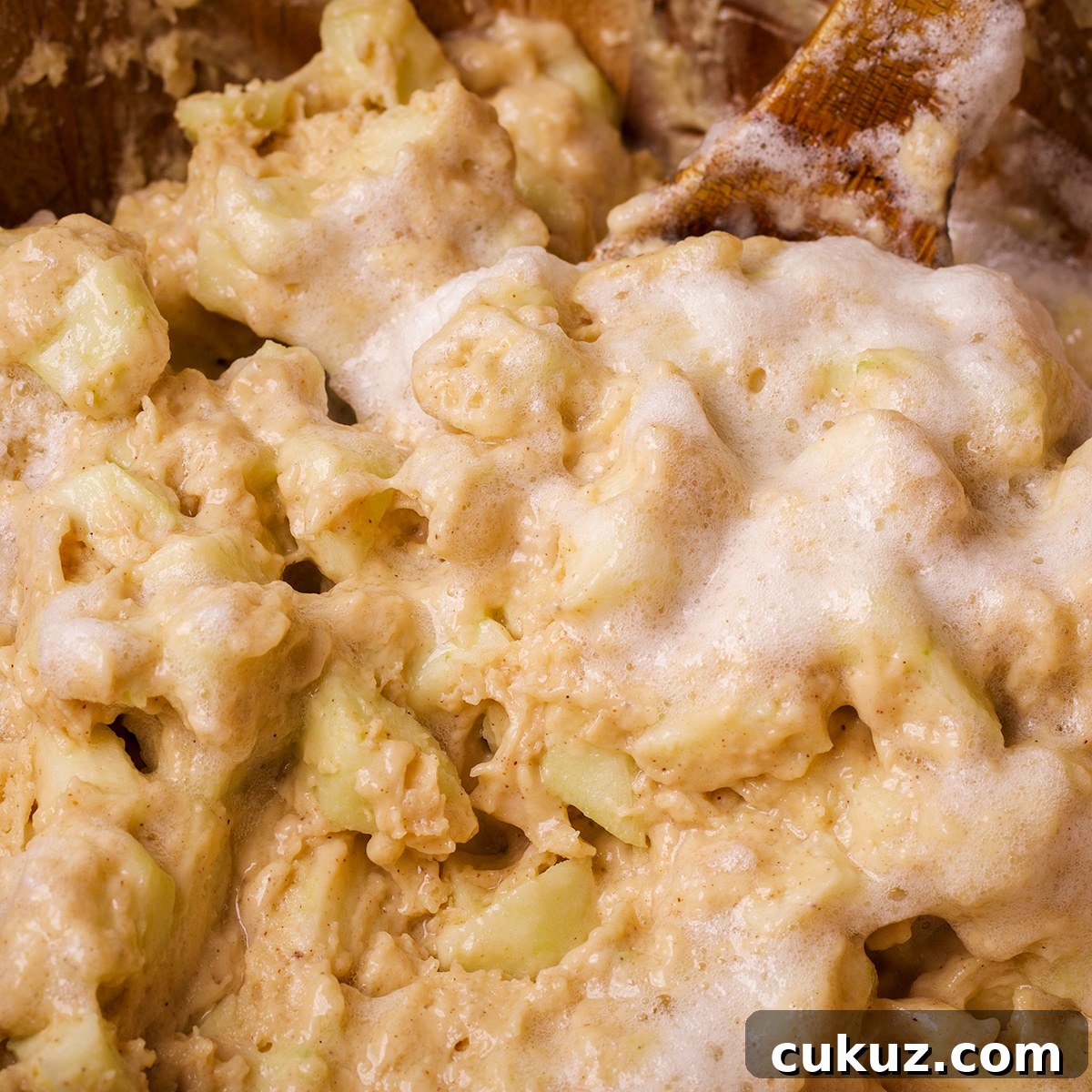 Someone using a wood spoon to fold beaten egg whites into the batter for Irish Apple Cake.