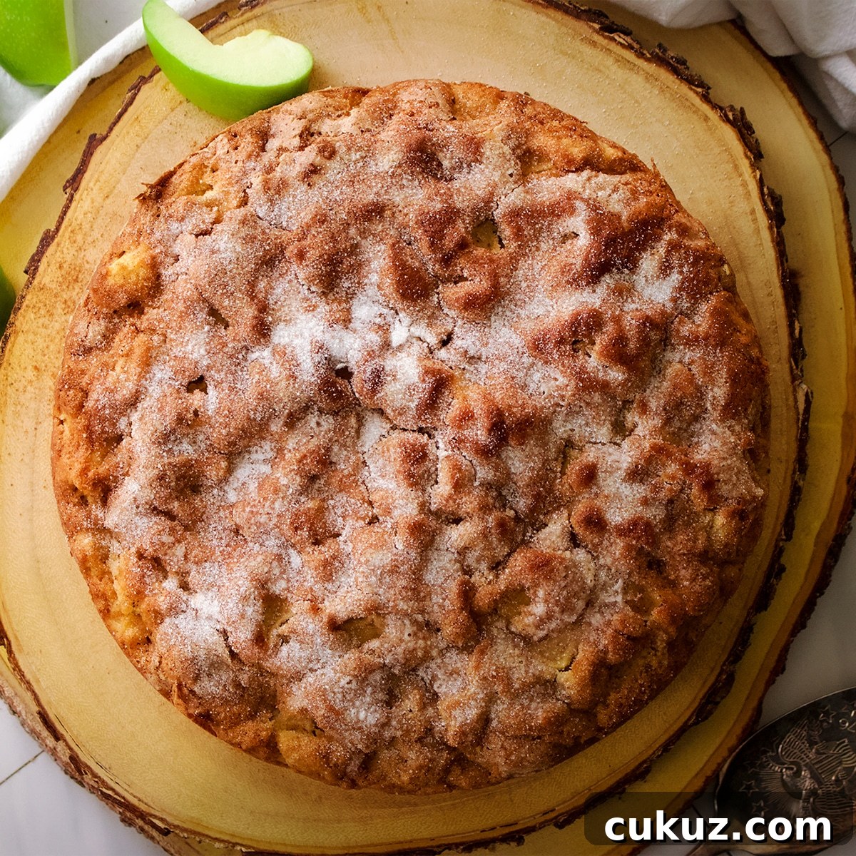 An Irish Apple Cake with a crunchy sugar coated top on a wood cake board with some sliced green apples.