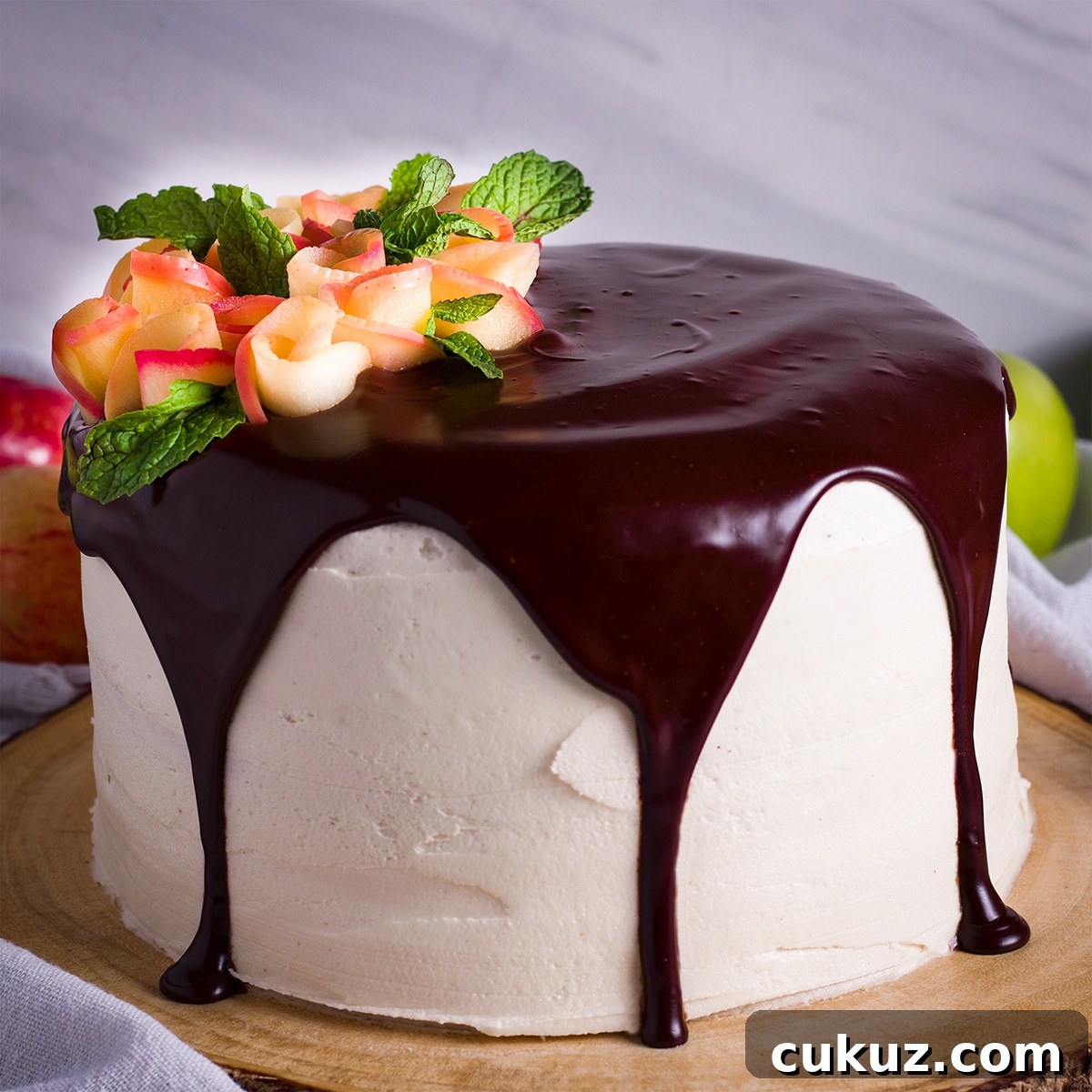 A frosted layer cake topped with chocolate ganache and decorated with apple roses.
