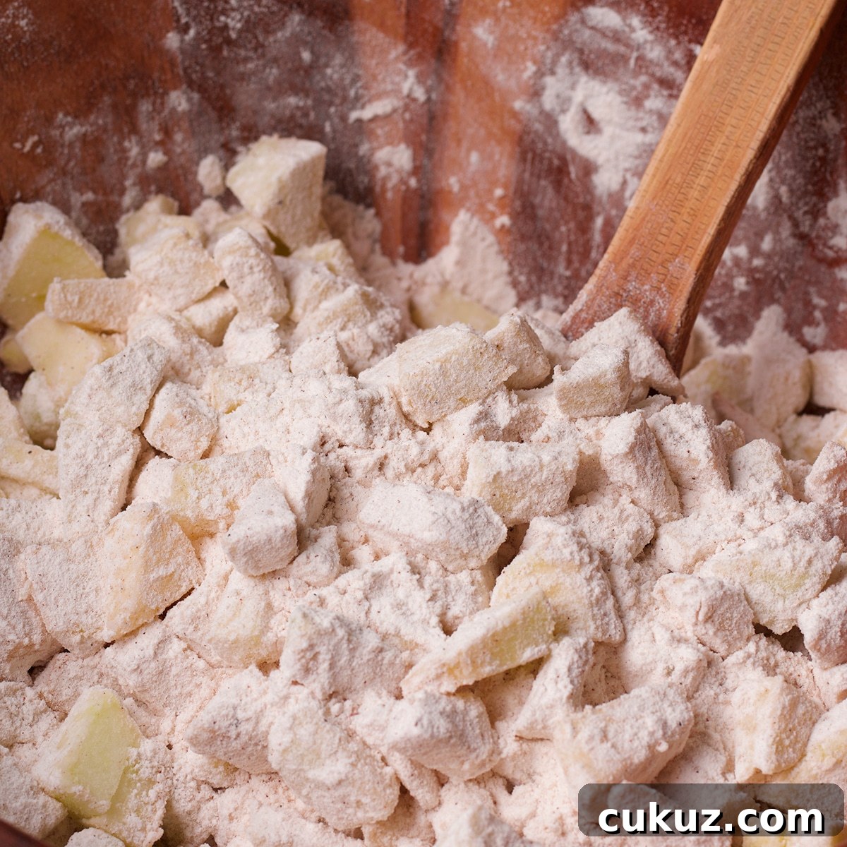 Using a wood spoon to stir chopped apples into flour.