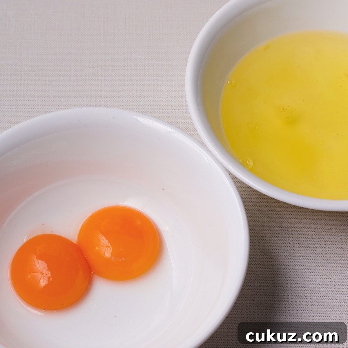Two white bowls with egg yolks in one and egg whites in another.