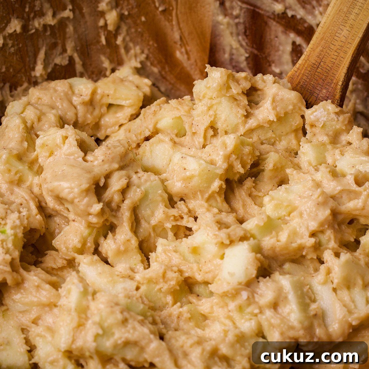 Someone using a wood spoon to stir Irish Apple Cake batter.