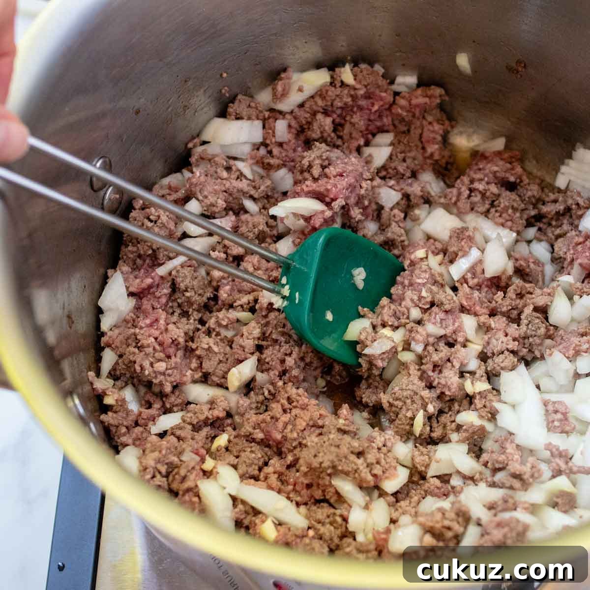 a large pot with ground beef, onions, and garlic cooking.