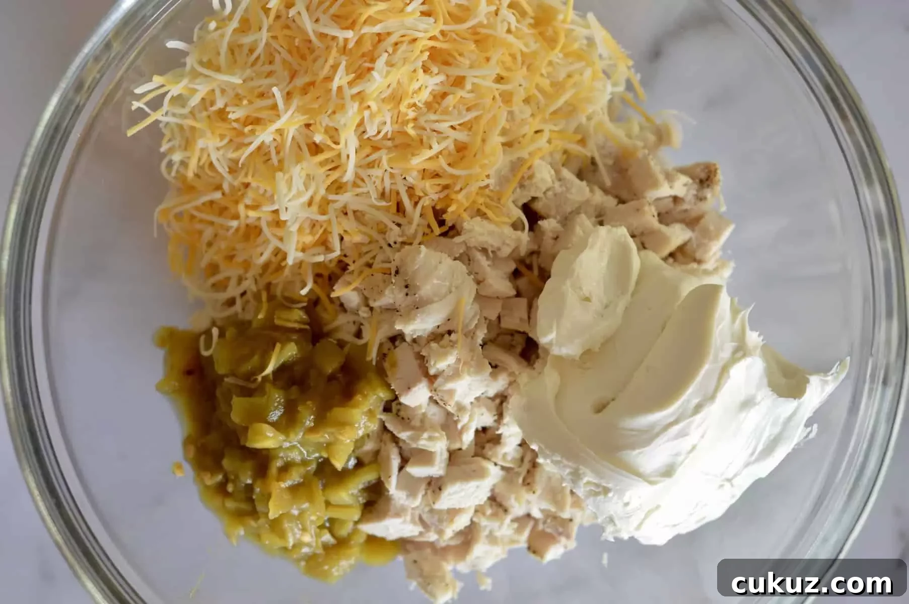 chicken in a bowl along with cream cheese, green chilis, and shredded cheddar cheese.