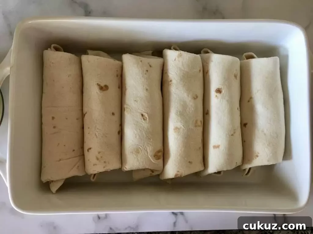 six burritos rolled in a white casserole dish.