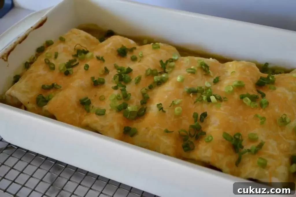Green Chili Chicken Burritos in a white casserole dish with green onions sprinkled over top.