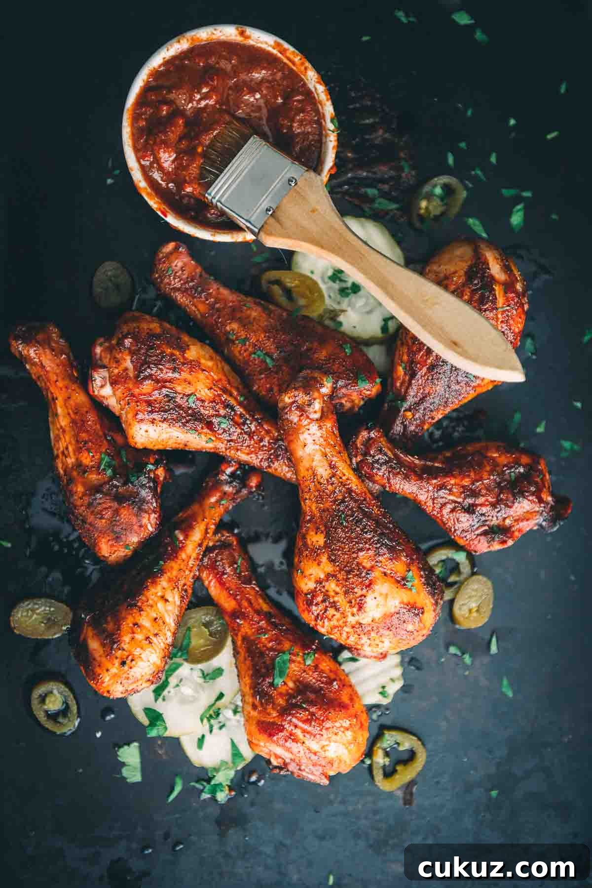 Overhead of smoked chicken drums showing golden bbq rubbed chicken skin on a black board with garnish.