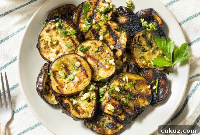 Perfectly Grilled Eggplant Recipe for Smoky Summer Flavor 4 charred eggplant slices served fresh from grill garnished in chopped garlic and parsley marinade