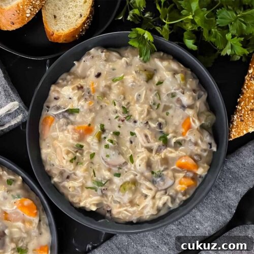 Slow cooker chicken and wild rice soup in a dark bowl with a cut loaf of crusty bread.