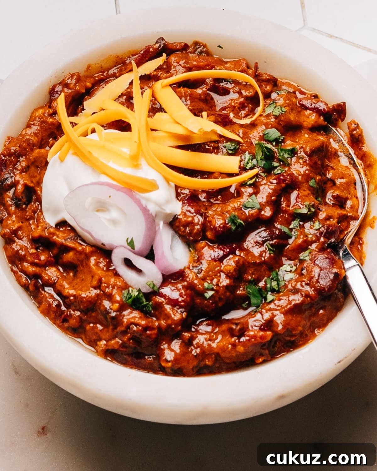 Turkey chili crockpot recipe in a bowl with sour cream, onions, and cheese.