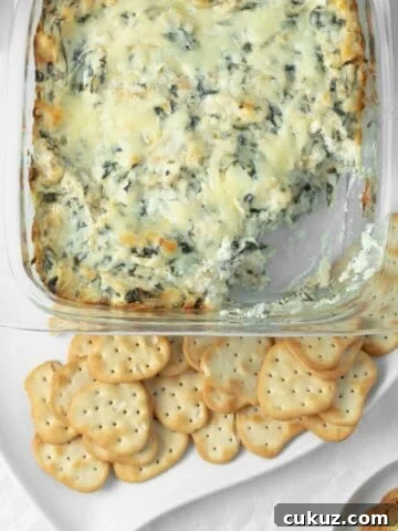 Baked spinach artichoke dip with a scoop taken out of it with crackers on a serving dish.