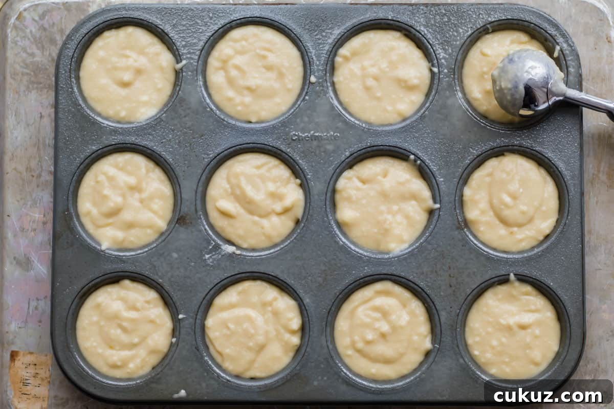 cookie scoop filling batter into a muffin tin