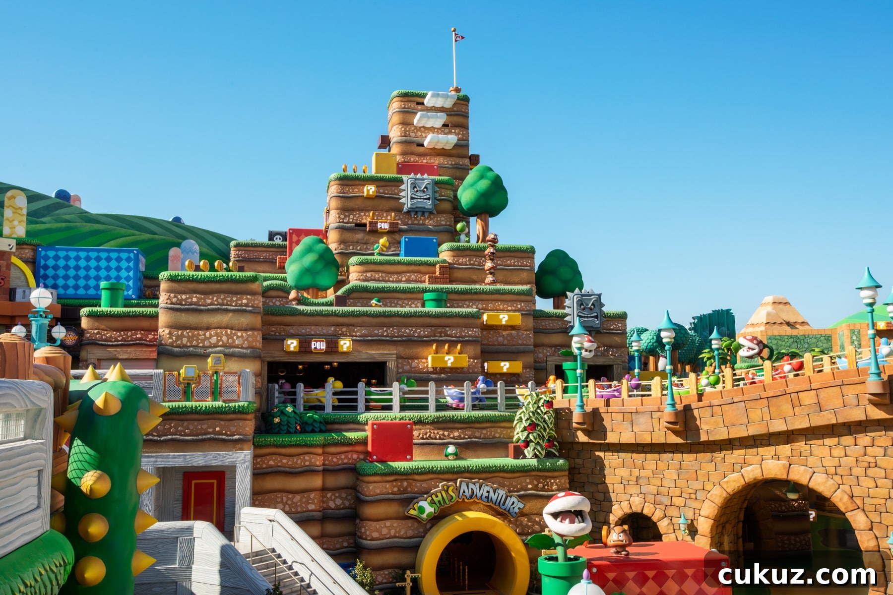 Colorful theme park area featuring a multi-level structure with blocky designs, green trees, and iconic question mark boxes inspired by Super Mario.
