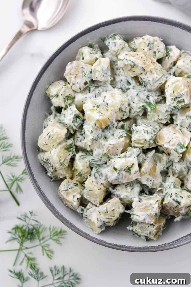 Creamy Herbed Potato Salad in a bowl next to a spoon and dill sprigs.