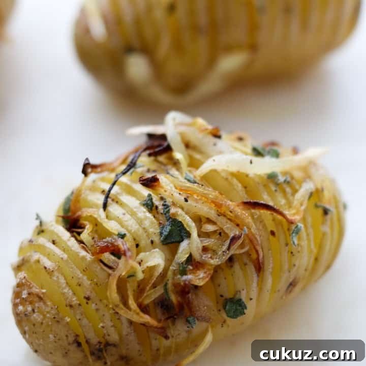 Close up of a hasselback potato topped with herbs and caramelized onions