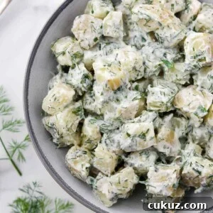 Creamy Herbed Potato Salad in a bowl next to a spoon and dill sprigs.