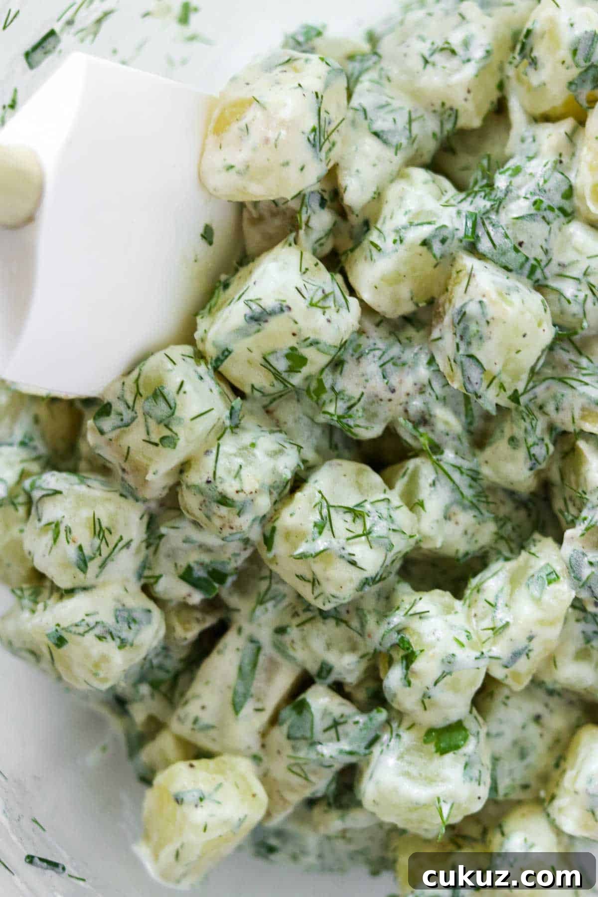 Rubber spatula stirring a creamy potato salad.