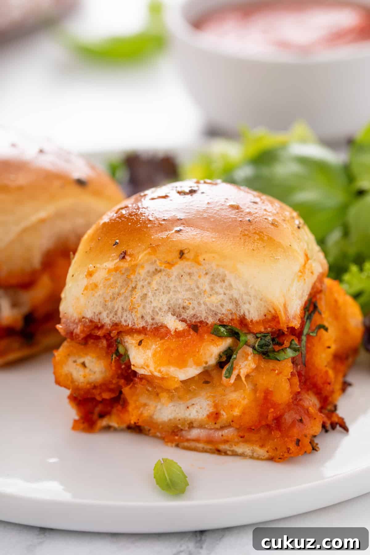 Chicken parmesan slider on a white plate with a green salad in the background.