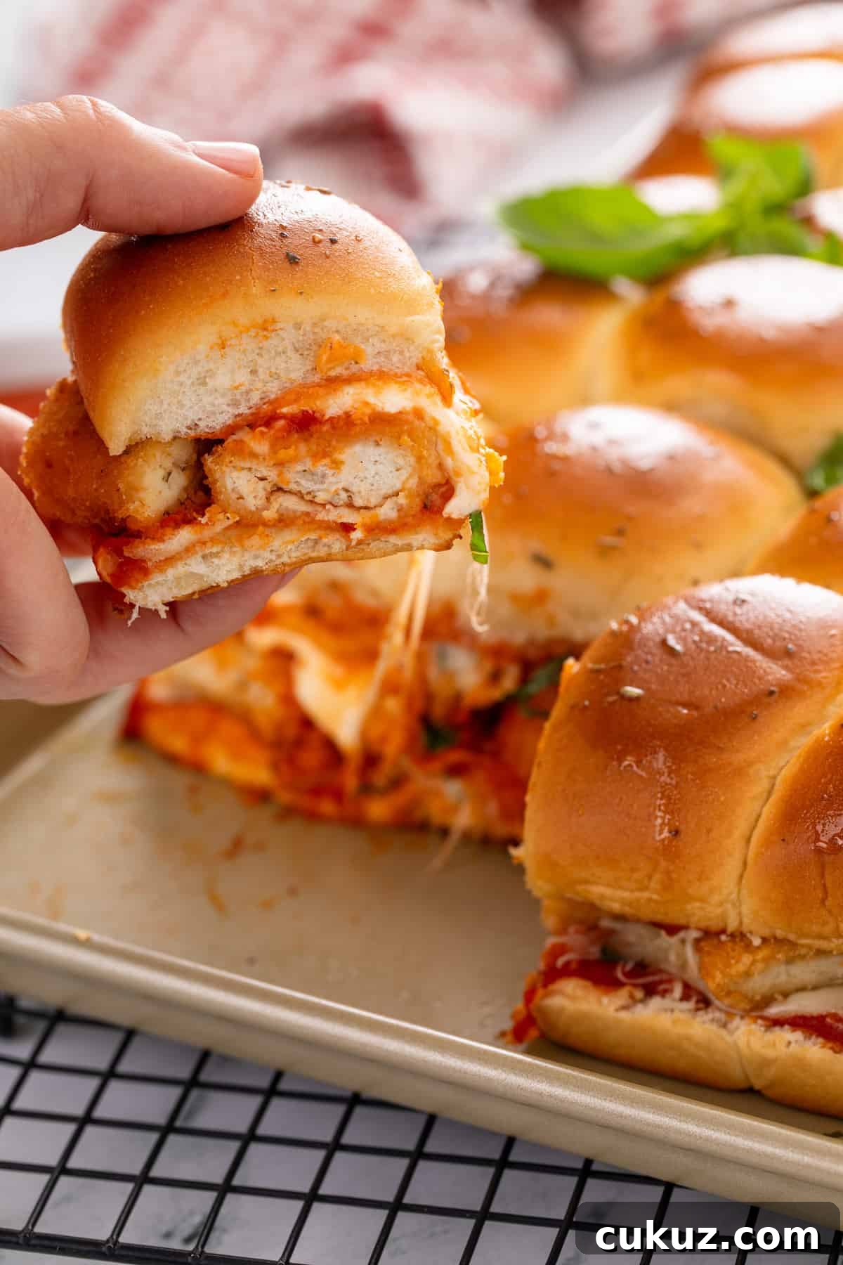 Hand picking up a chicken parmesan slider from the pan of sliders.
