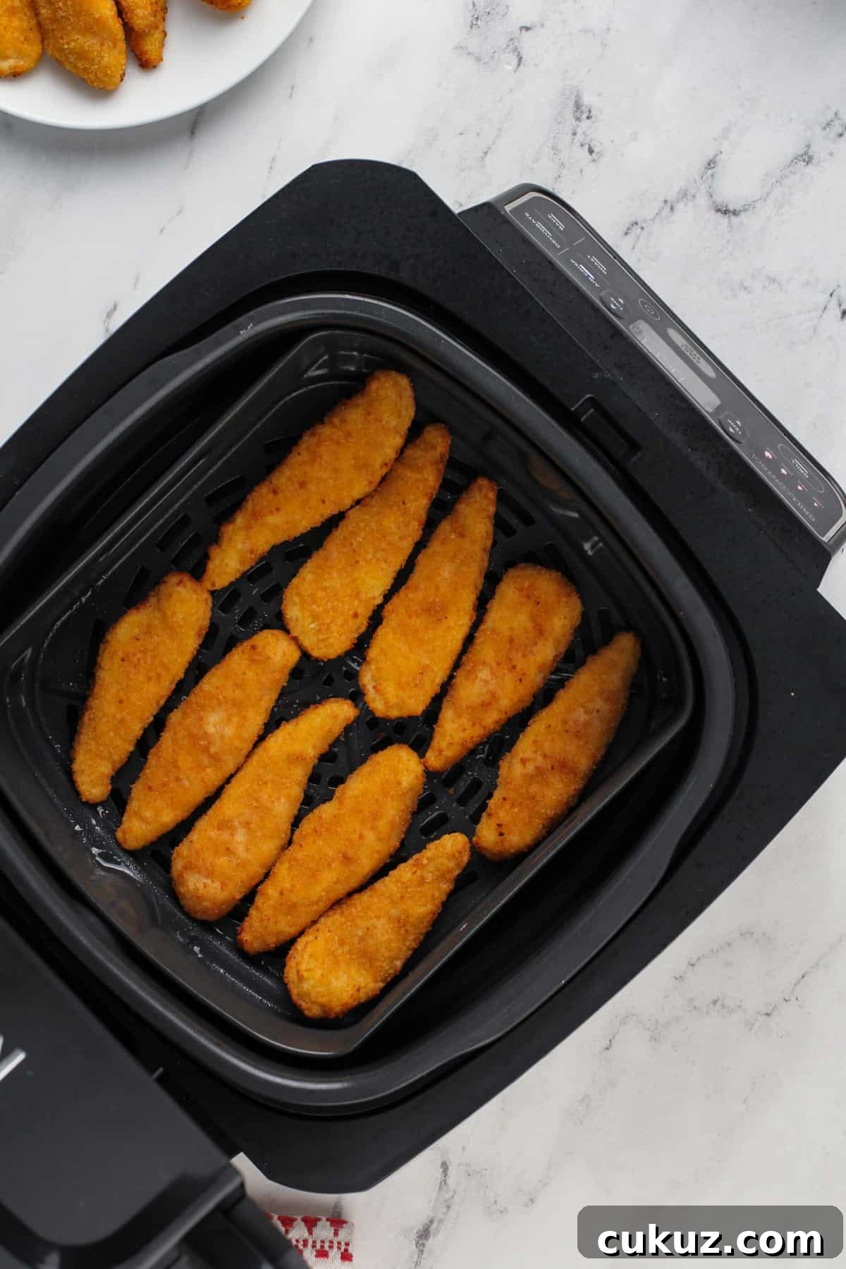 Cooked chicken tenders in the basket of an air fryer.