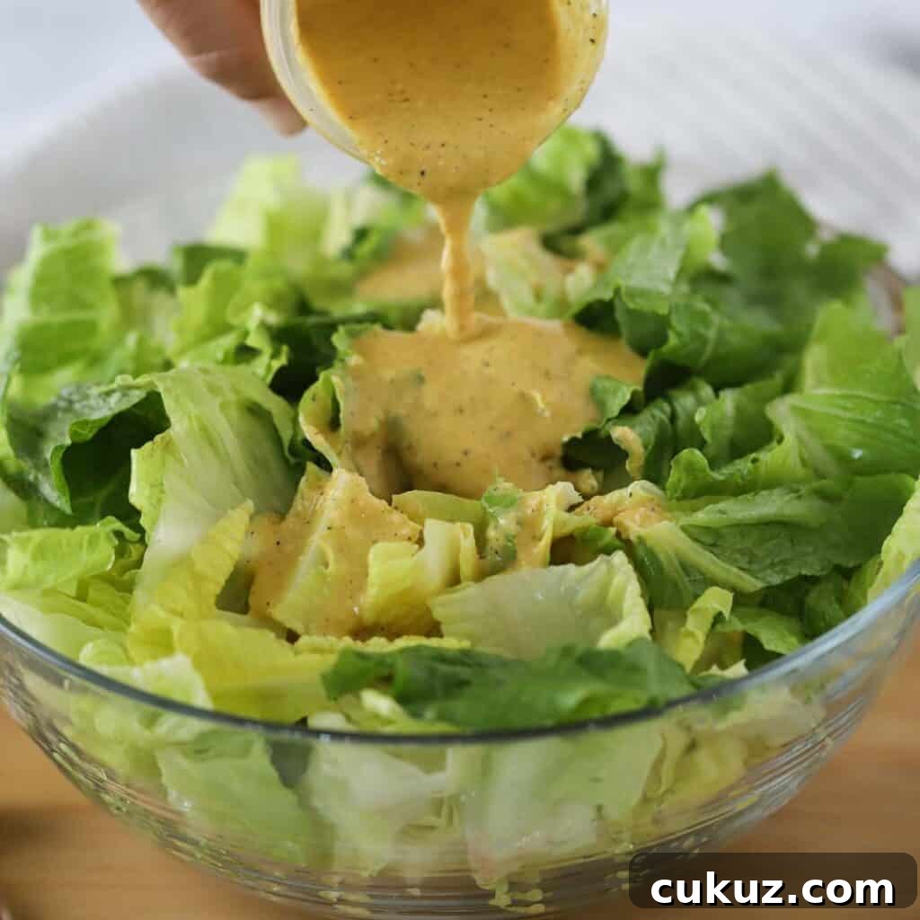 Creamy caesar dressing being poured over a large salad bowl full of romaine lettuce. 