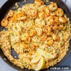 top view risotto in black skillet topped with shrimp in a black skillet with 3 lemon wedges to garnish