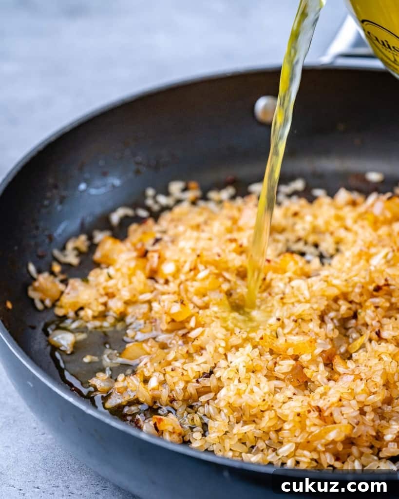 broth being poured over seasoned rice in a skillet to make risotto