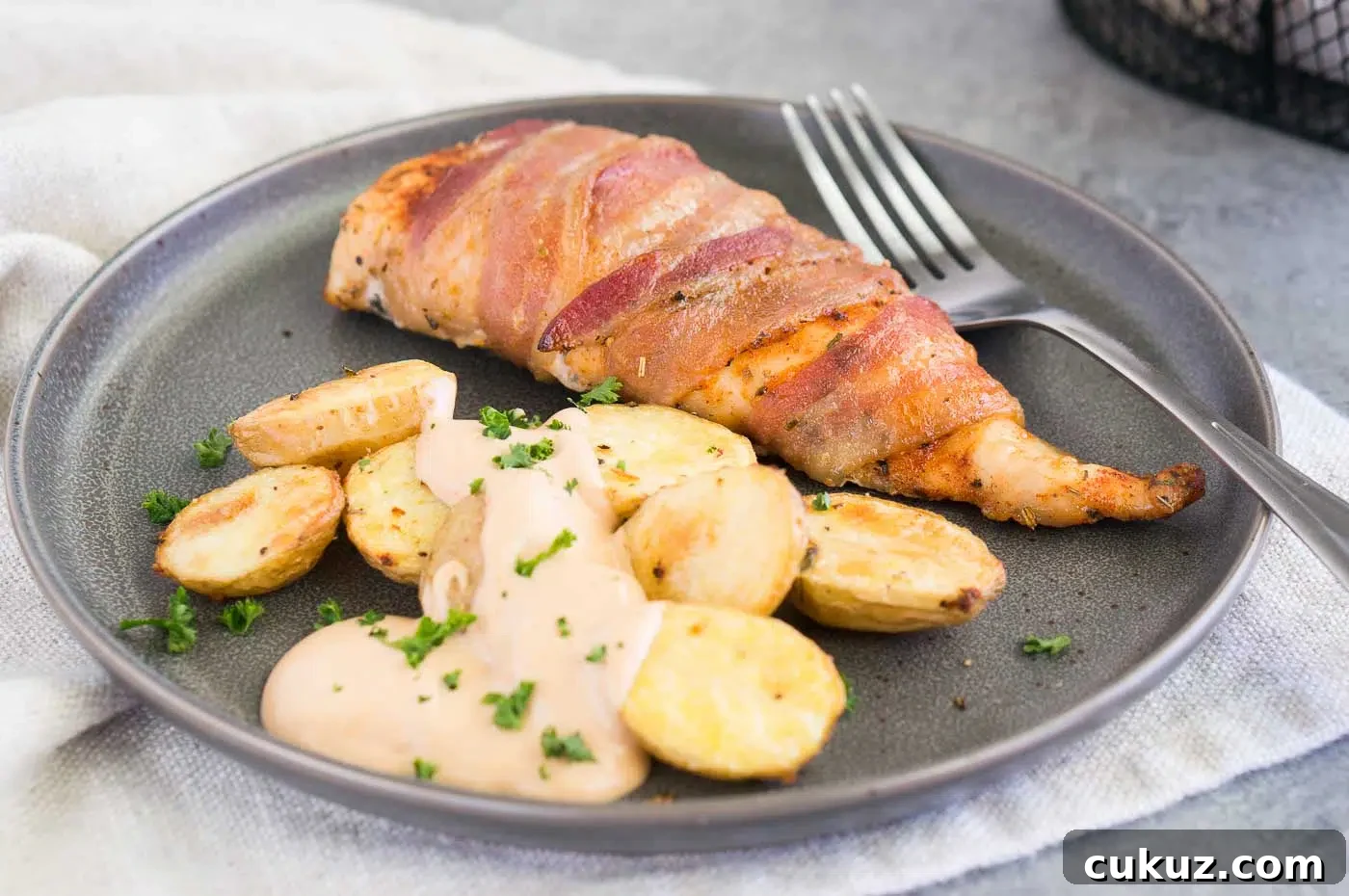 close up image of chicken wrapped in bacon with roasted potatoes on a plate 