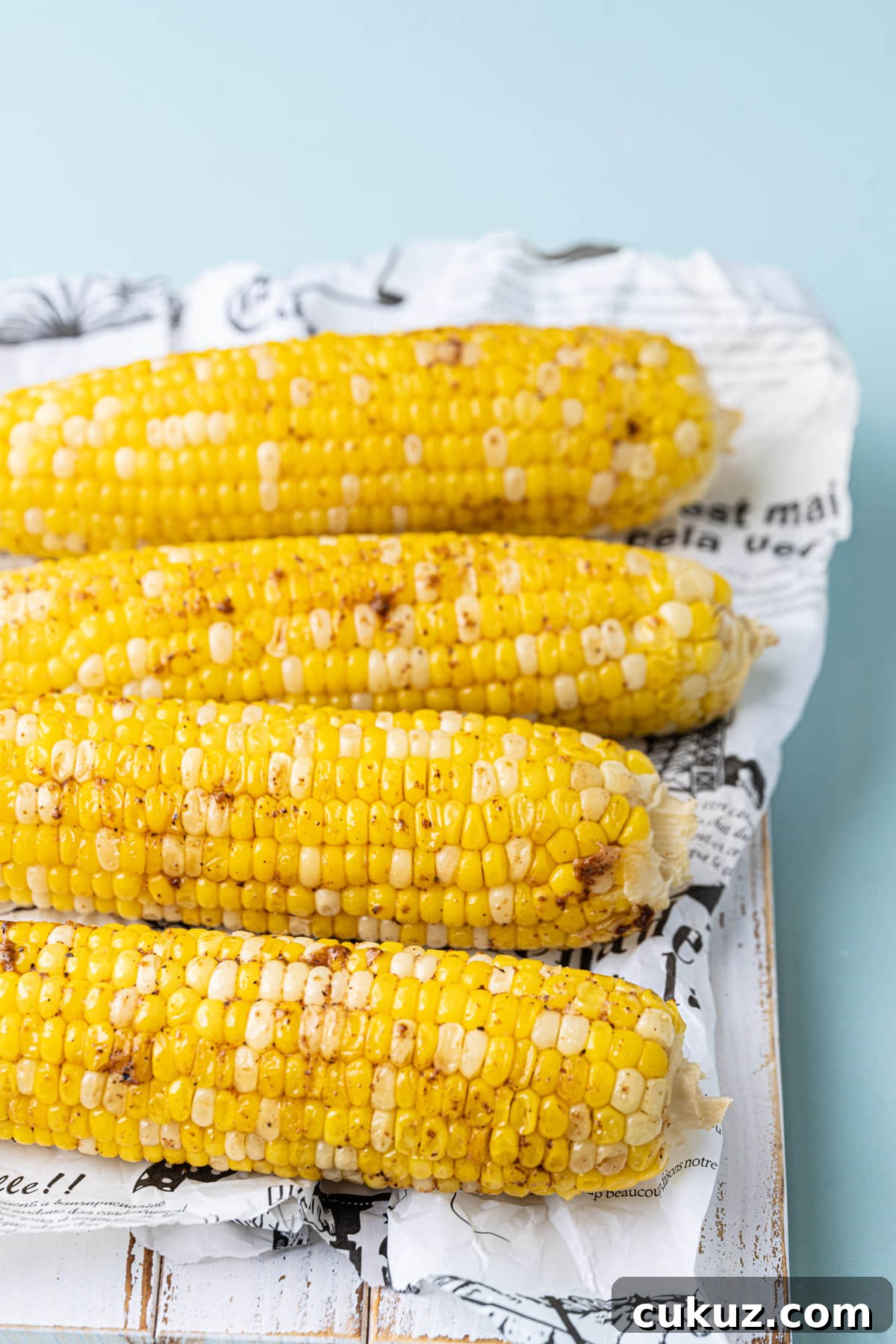 4 ears of roasted corn sprinkled with Cajun seasoning lined up on a board.