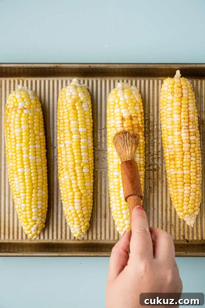 Brushing Cajun butter onto corn on the cob before roasting it in the oven. 