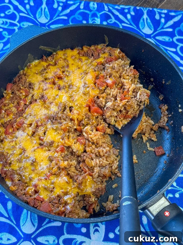 One-Pan Taco Rice Skillet Recipe for Quick Weeknight Dinners 12 Serving spoon full of a tender and delicious Mexican beef and rice skillet meal on a blue and white napkin.
