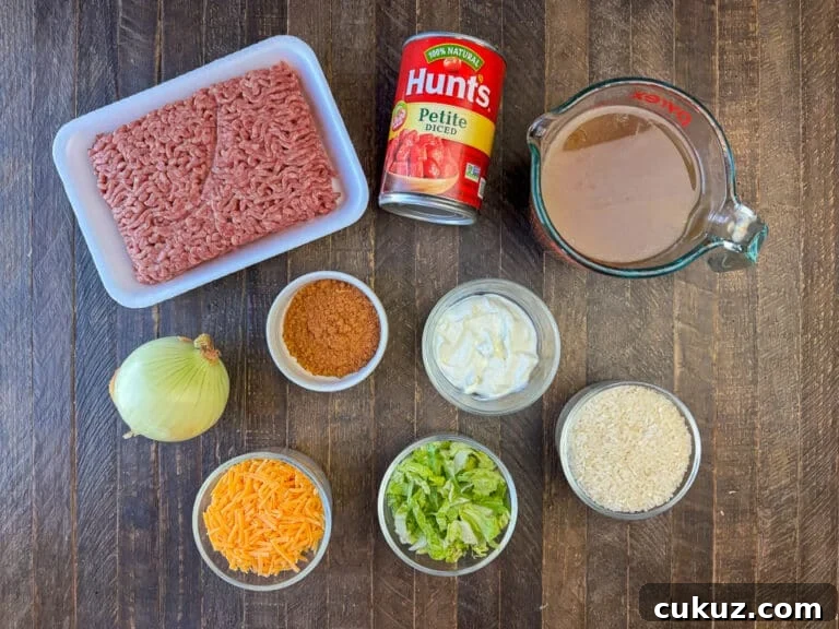 One-Pan Taco Rice Skillet Recipe for Quick Weeknight Dinners 4 Ingredients to make a Mexican beef rice skillet are ground beef, petite diced tomatoes, beef broth, onion, taco seasoning, sour cream, rice, lettuce and cheddar cheese on a wooden counter top.