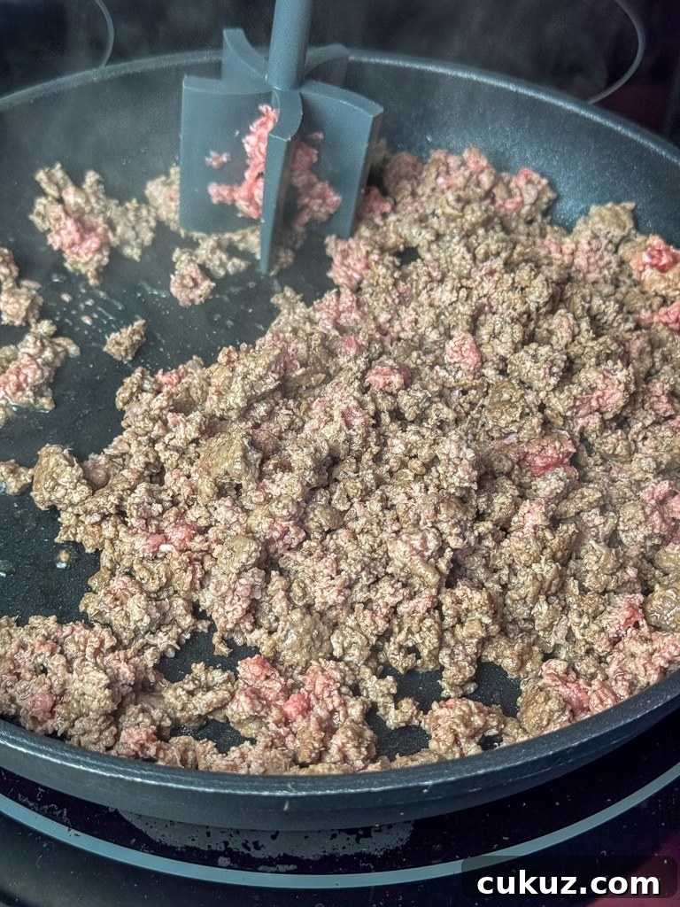 One-Pan Taco Rice Skillet Recipe for Quick Weeknight Dinners 5 Meat masher breaking up hamburger to cook the pink out in a black skillet.