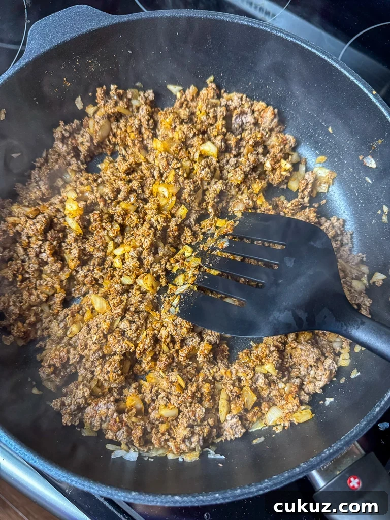 One-Pan Taco Rice Skillet Recipe for Quick Weeknight Dinners 6 Spatula stirring taco seasoning into cooked ground beef and onions in a skillet.