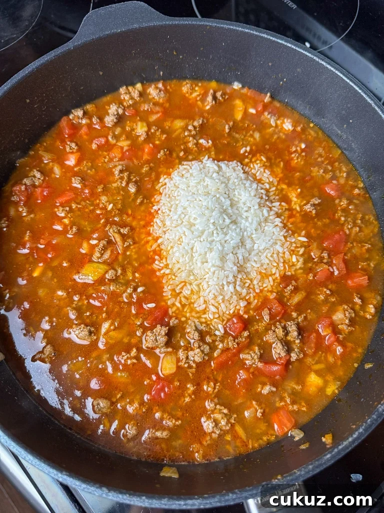 One-Pan Taco Rice Skillet Recipe for Quick Weeknight Dinners 8 Raw rice poured into a skillet with cooked ground beef, tomatoes and broth with a generous amount of taco seasoning.