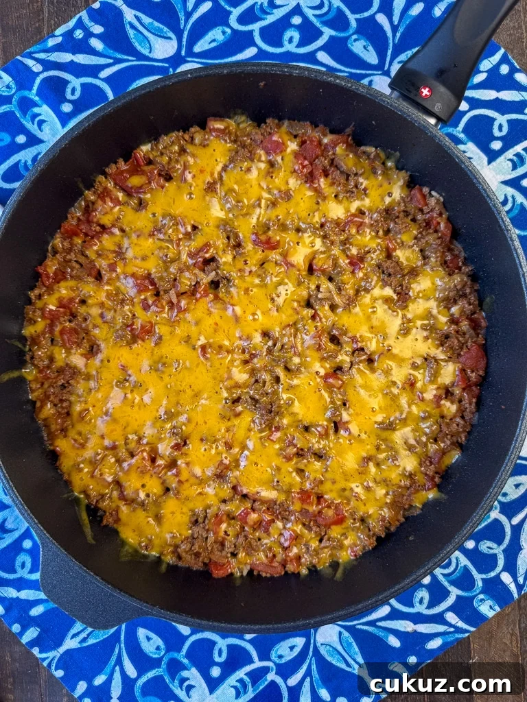 One-Pan Taco Rice Skillet Recipe for Quick Weeknight Dinners 10 Overhead view of a flavorful cheesy Mexican beef and rice one pot meal in a skillet on a blue and white napkin.
