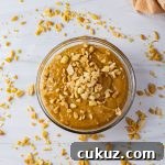 bowl of peanut butter sauce with chopped peanuts on top