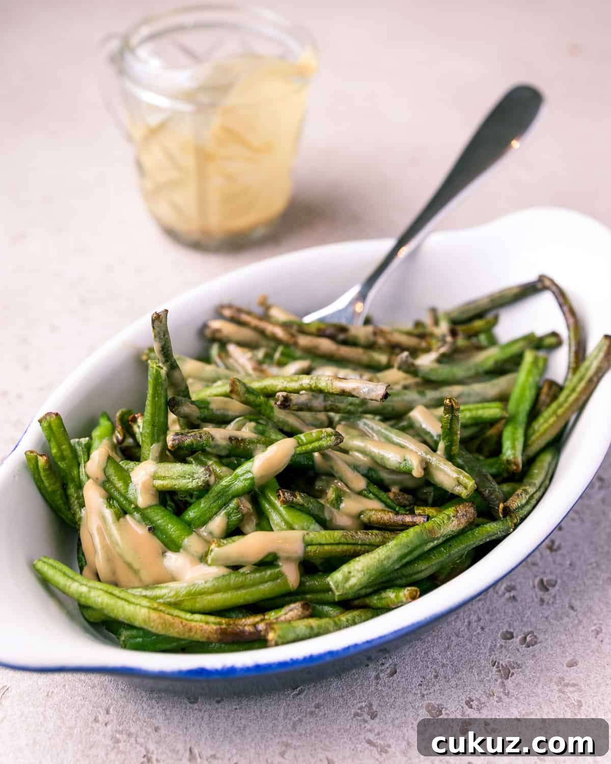 Photo of a dish of air fried green beans mixed with tahini and tamari sauce.