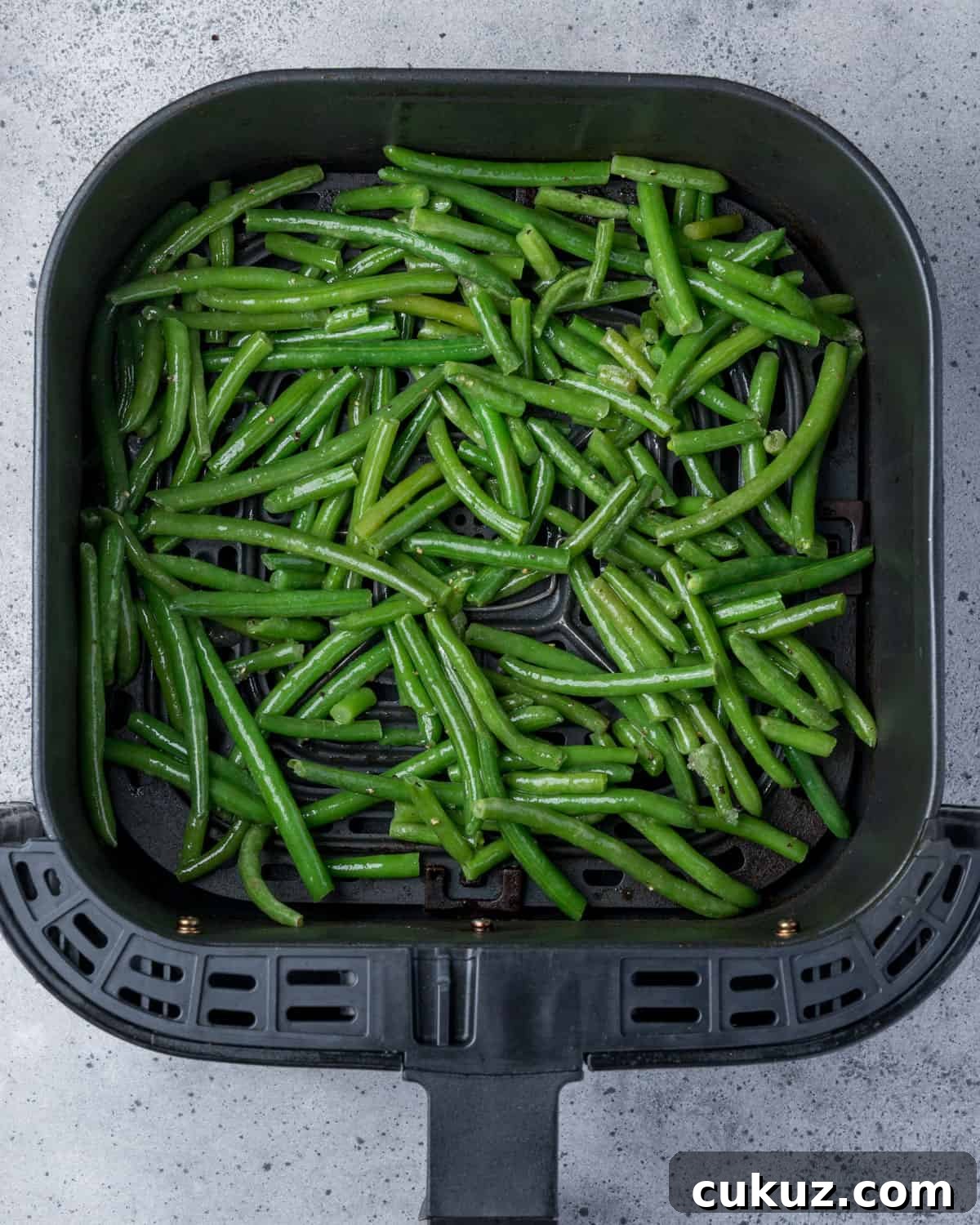 Photo showing uncooked green beans in the air fryer basket in a single layer.
